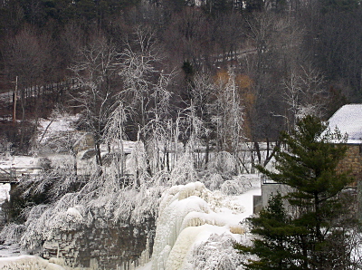 [A closer view of the leafless trees with snow piles on all the limbs just above the waterfall.]